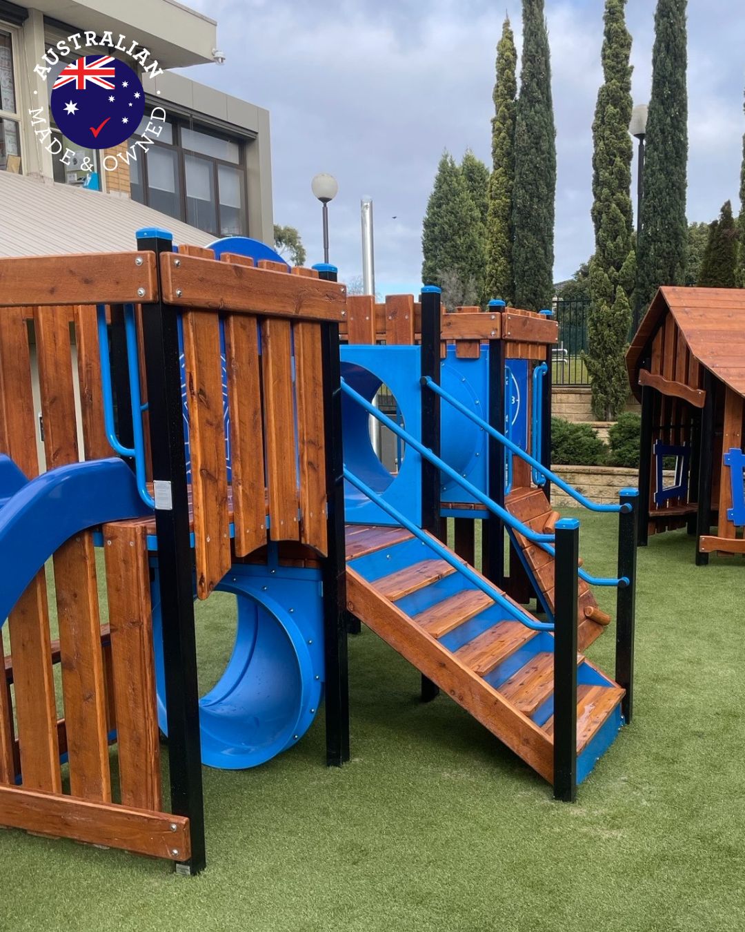 Fortitude Early Years Honeyeater Combination Unit featuring natural timber panels, bright blue slides, stairs, and crawl tunnel. Designed for early learning centres, the play structure combines durable Australian steel with warm timber, encouraging climbing, sliding, and imaginative play in a safe, engaging environment.