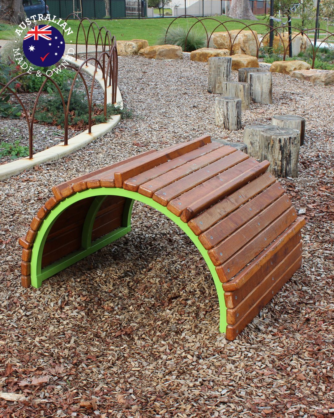 Timber arched climber from the Instinctive range, crafted from Australian hardwood with green steel frame, set in a natural playground with log steppers and landscaping.